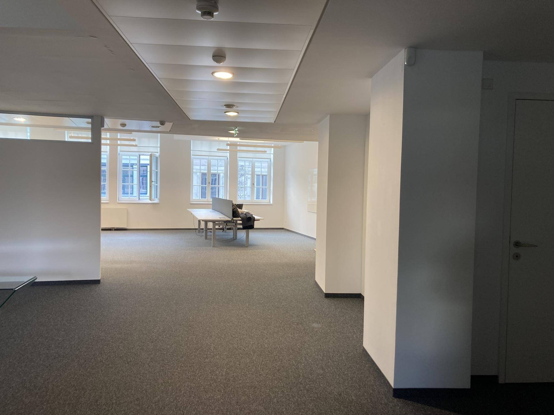 Geräumiges, leeres Büro mit Teppichboden, großen Fenstern und viel natürlichem Licht.