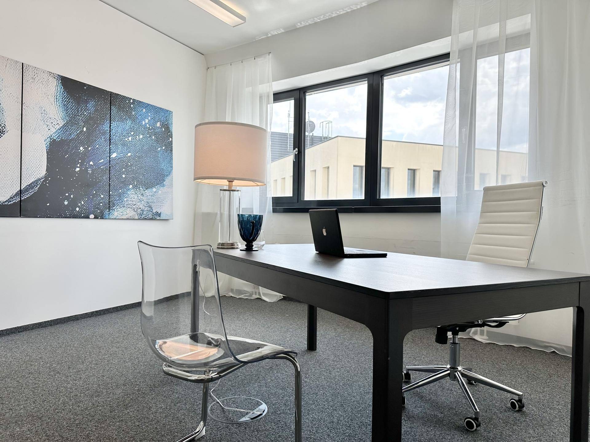 Einzelner Arbeitsplatz mit Schreibtisch, Bürostuhl und Kunstwerk an der Wand in einem hellen Büro.