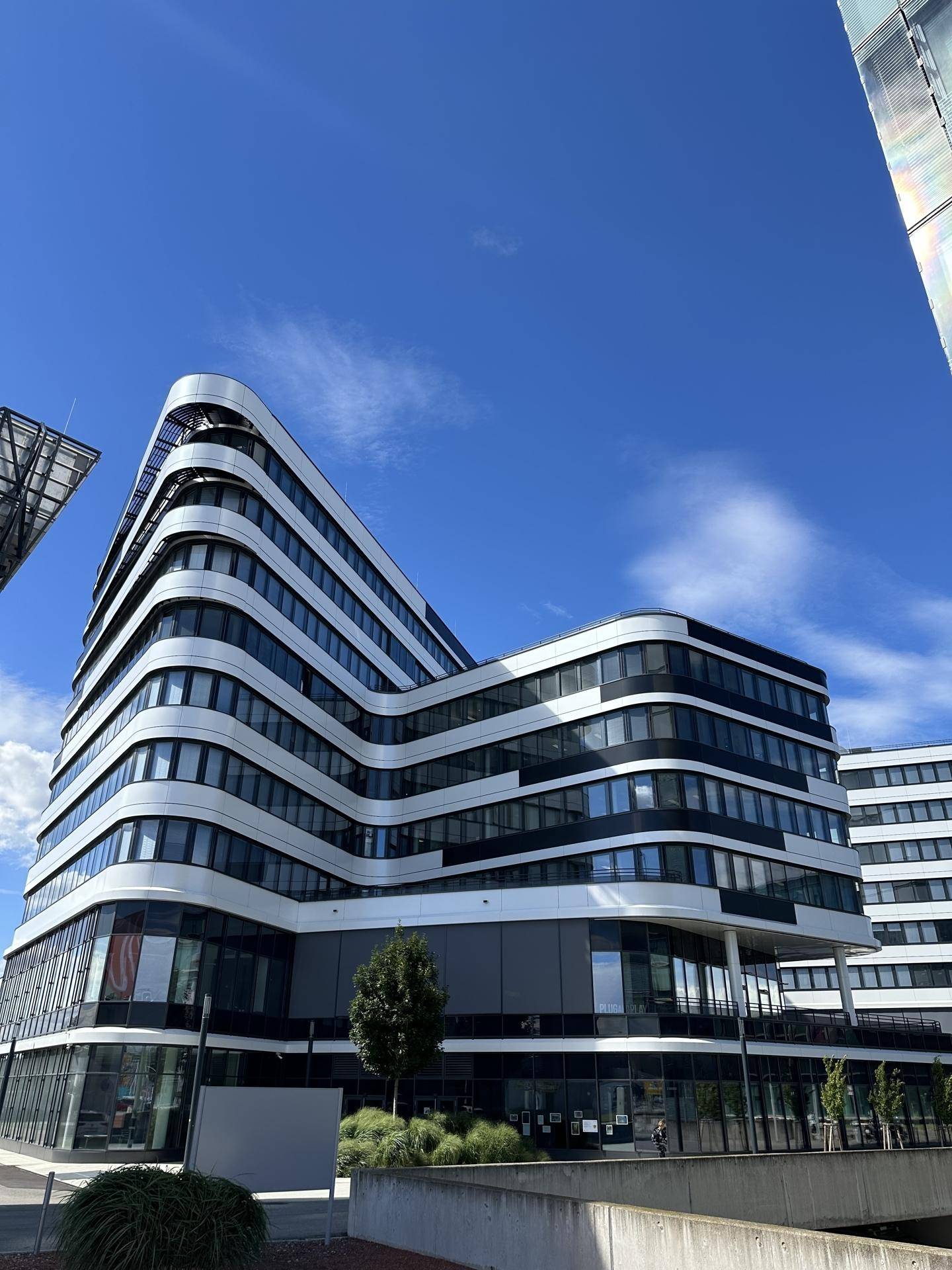 Ansicht eines modernen Bürogebäudes mit geschwungenen Linien und großen Fensterfronten unter blauem Himmel.