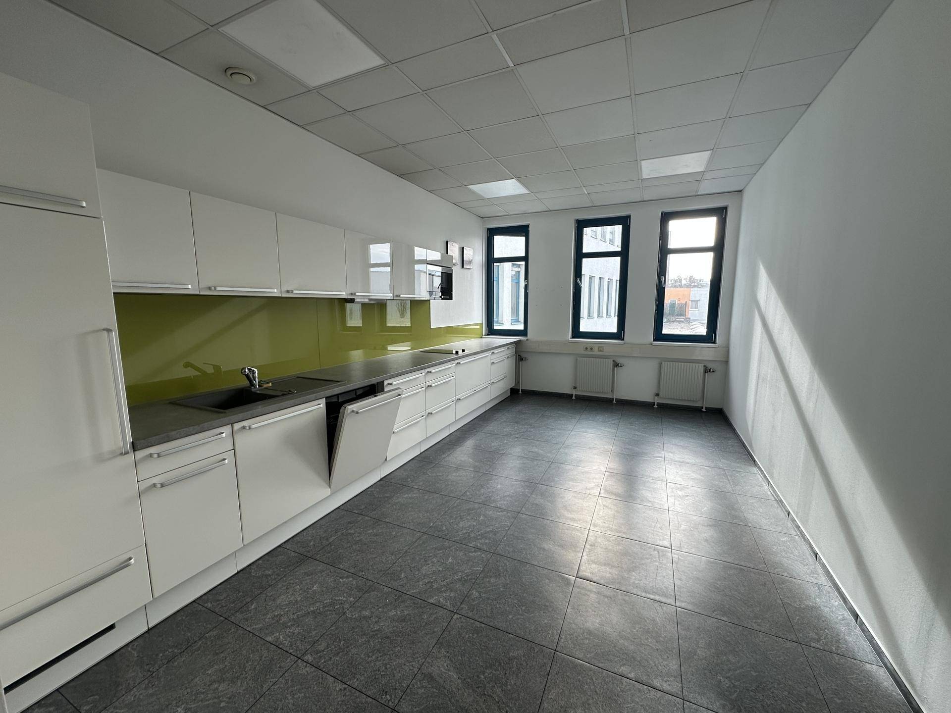 Moderne Einbauküche mit weißen Schränken, grüner Rückwand und Fliesenboden.