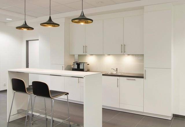 Moderne Teeküche mit weißen Schränken, dunkler Arbeitsplatte und Bartheke mit Hockern.