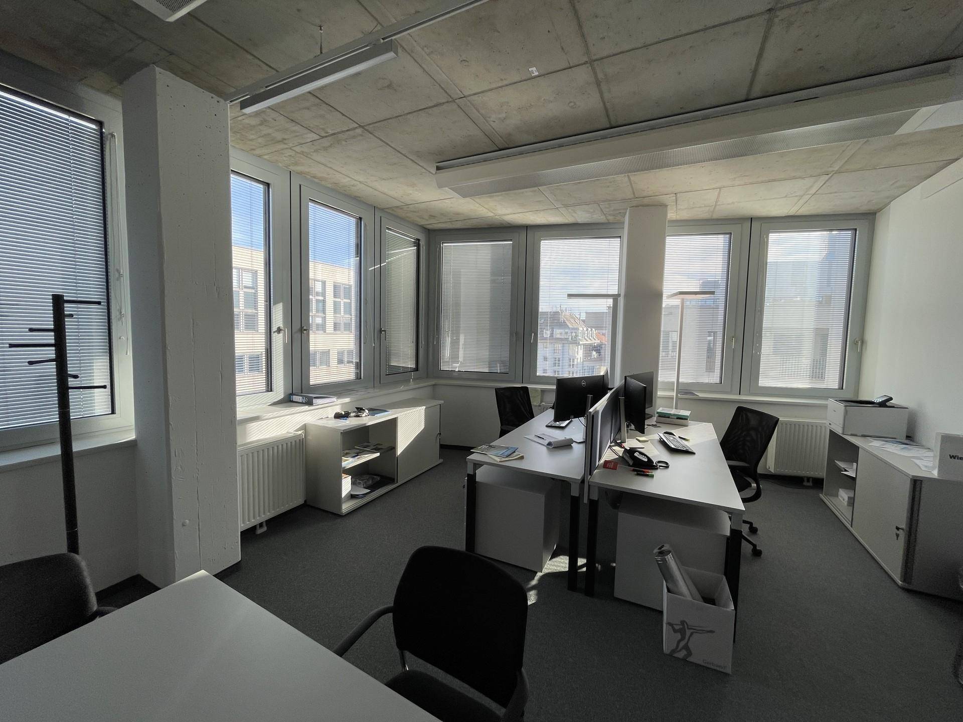 Helles Büro mit mehreren Arbeitsplätzen, großen Fenstern und Blick auf die Stadt.