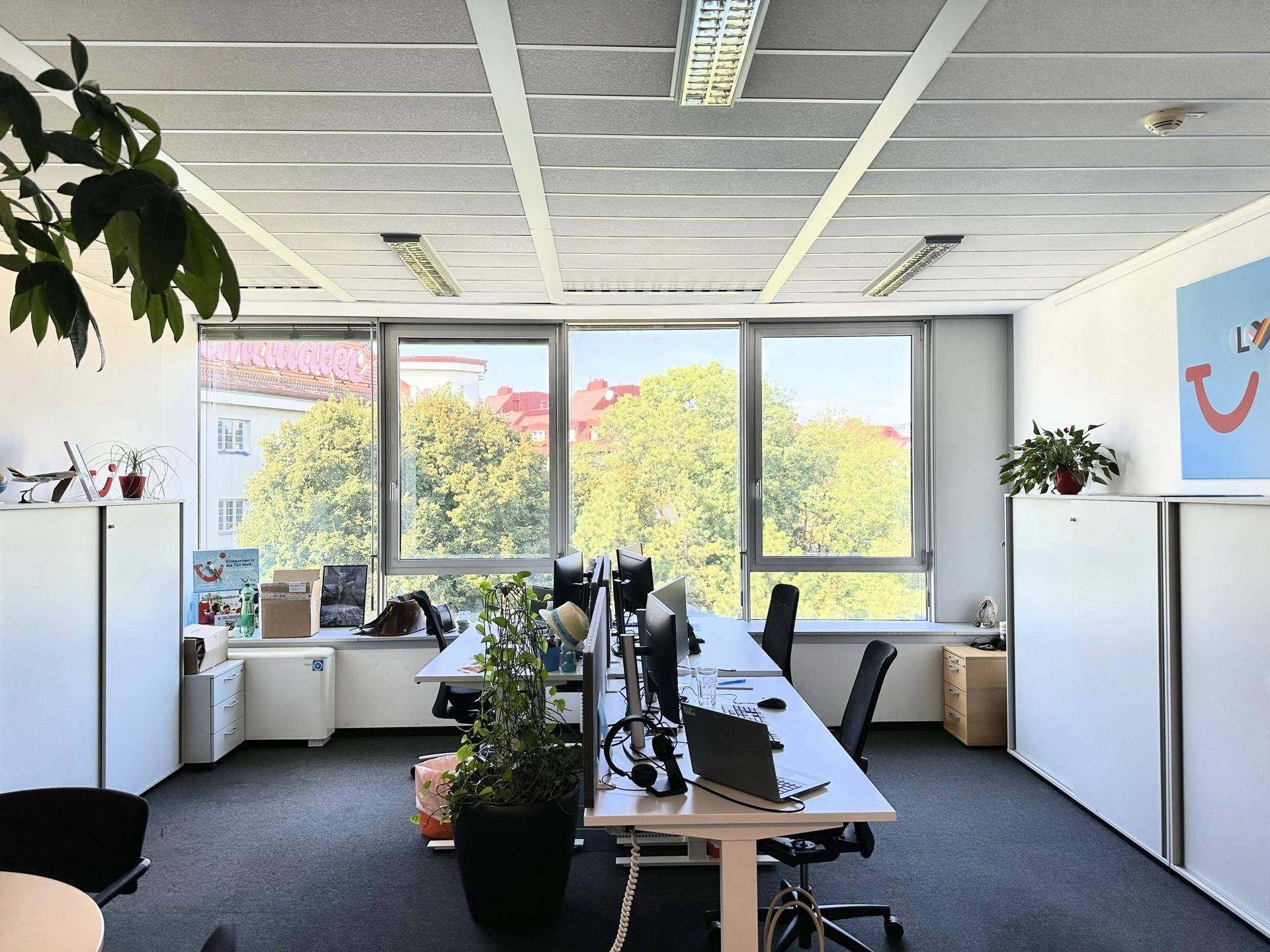 Helles Büro mit mehreren Arbeitsplätzen, großen Fenstern und Blick ins Grüne, ausgestattet mit Teppichboden.