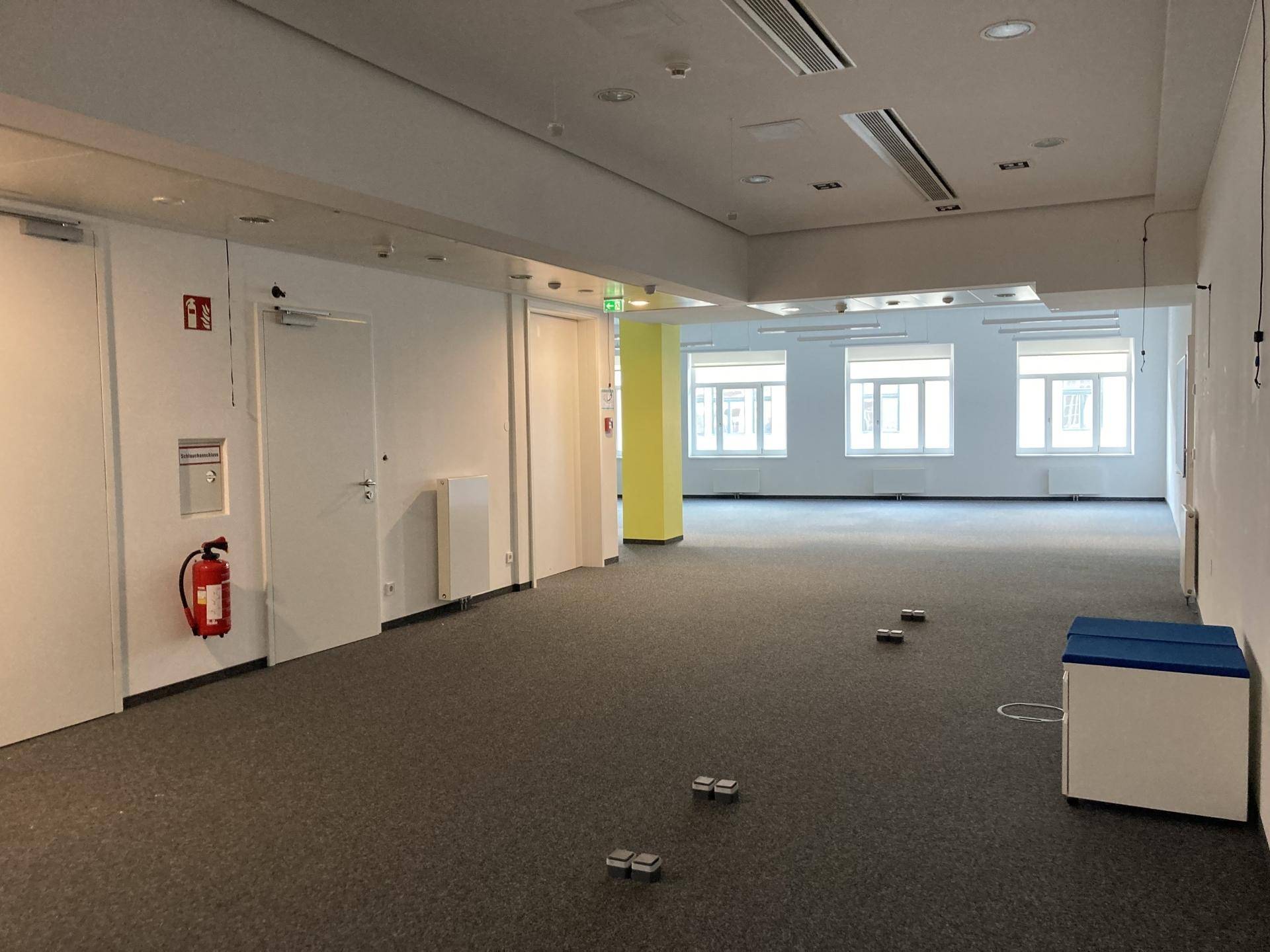 Weitläufiges Büro mit Teppichboden, weißen Wänden und einem auffälligen gelben Pfeiler.