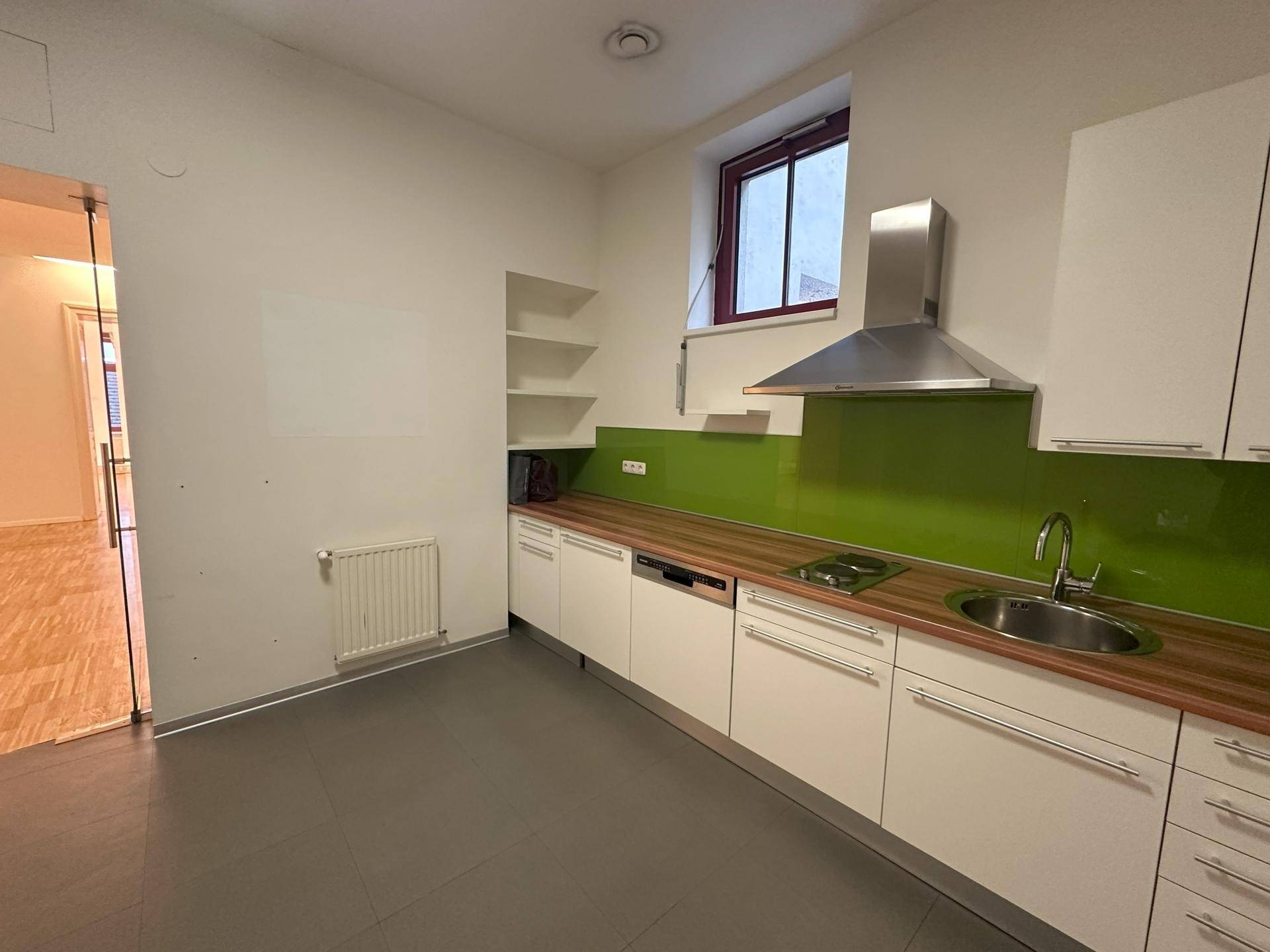 Kleine Einbauküche mit weißen Schränken, Holztheke und leuchtend grünem Fliesenspiegel.