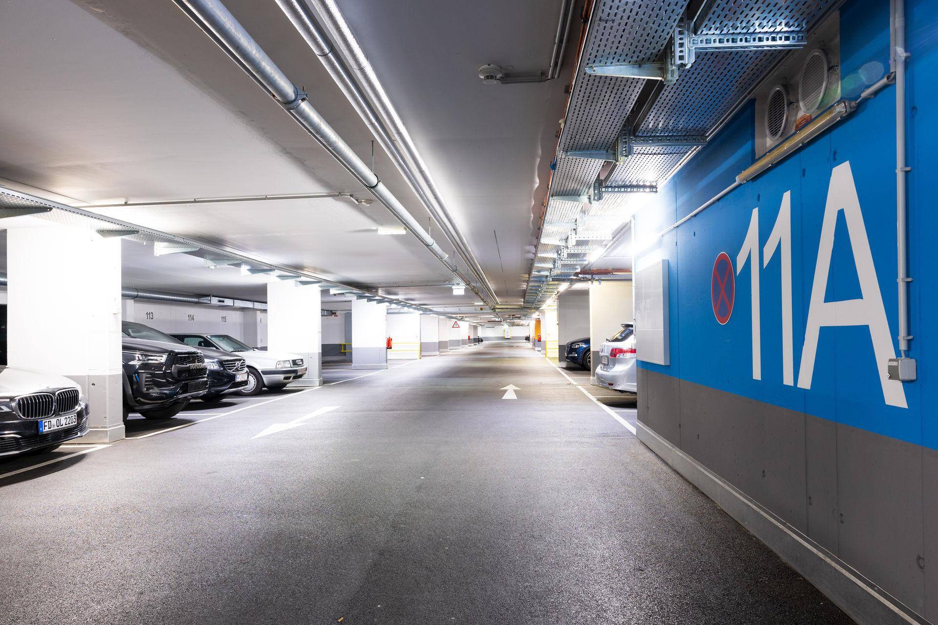 Geräumige Tiefgarage mit vielen Parkplätzen, Betonpfeilern und sichtbaren Installationen an der Decke.