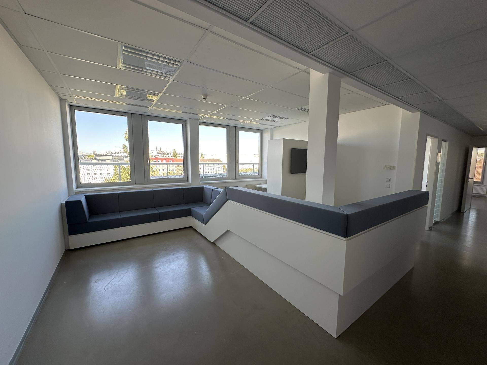 Moderner Empfangsbereich mit einer blauen Sitzbank, großen Fenstern und Blick auf die Stadt.