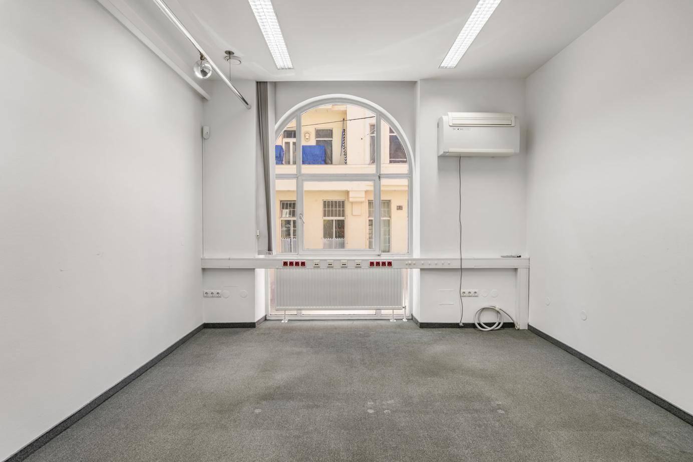 Leerer Büroraum mit Teppichboden, Rundbogenfenster und Klimaanlage.