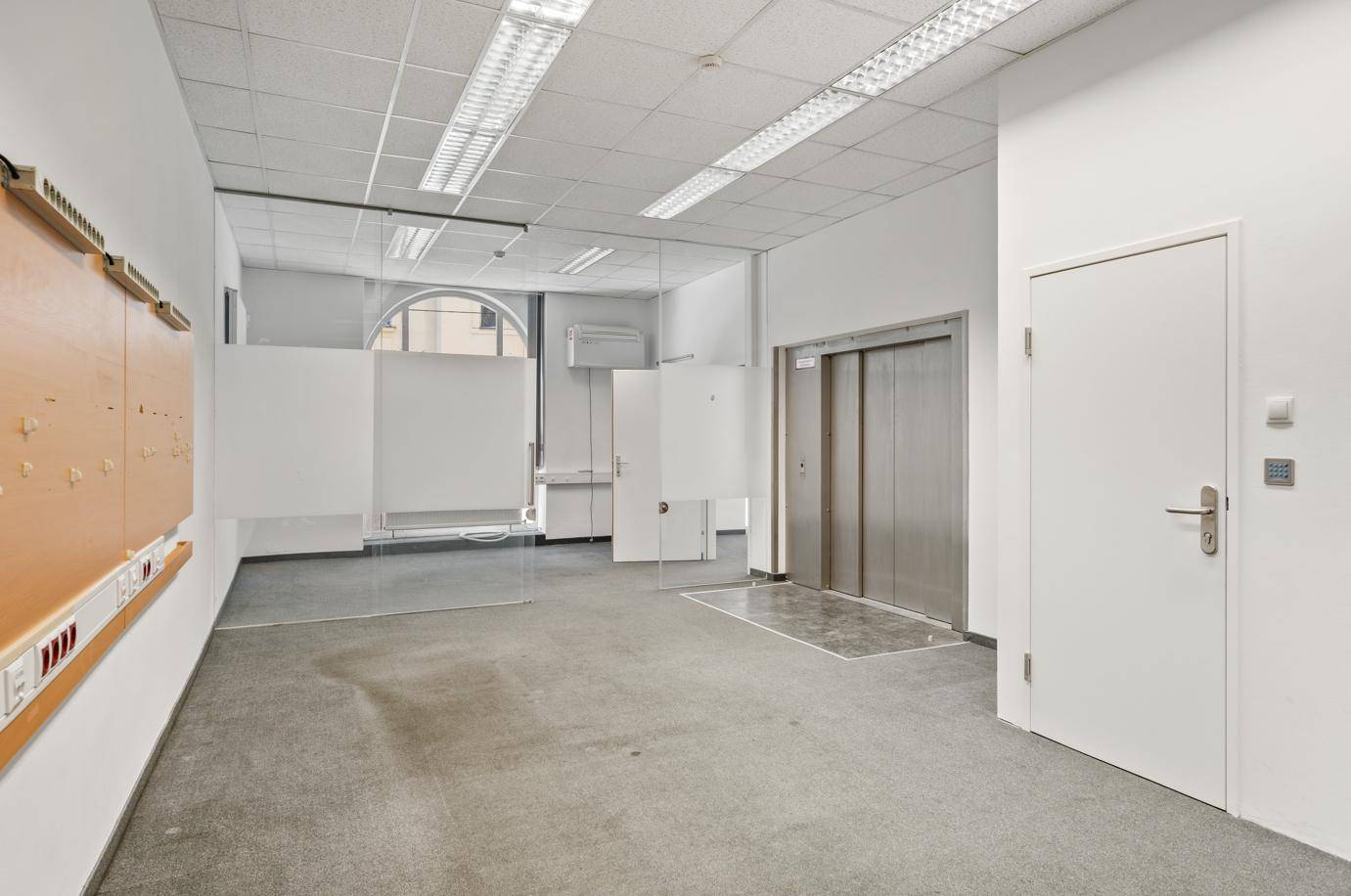 Heller Bürobereich mit Teppichboden, Glaswänden und Aufzug.