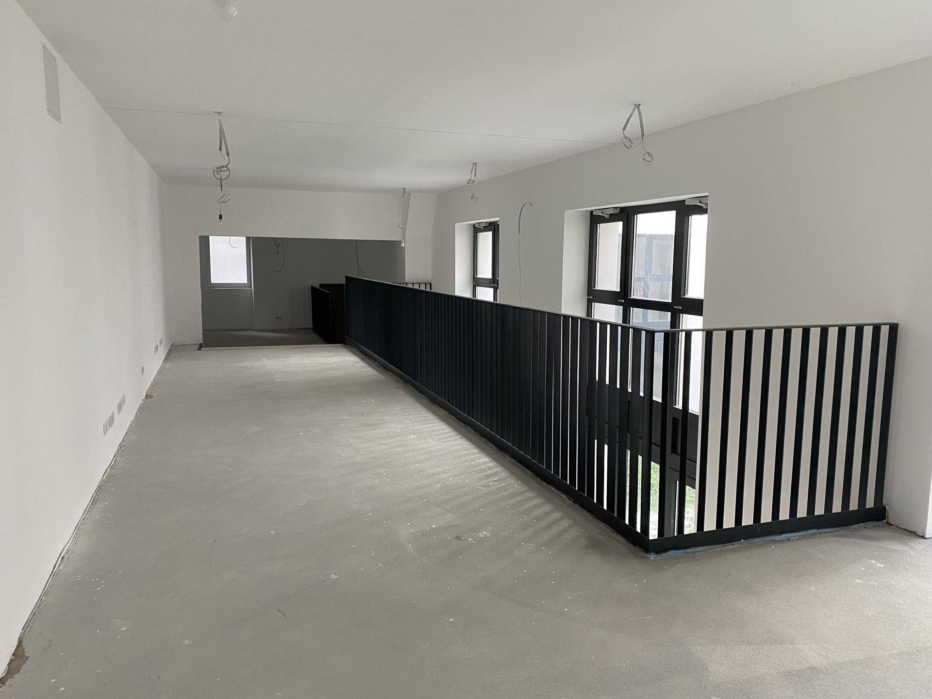 Weiterer Blick in den offenen Innenraum mit Betonboden, weißen Wänden und schwarzem Metallgeländer.