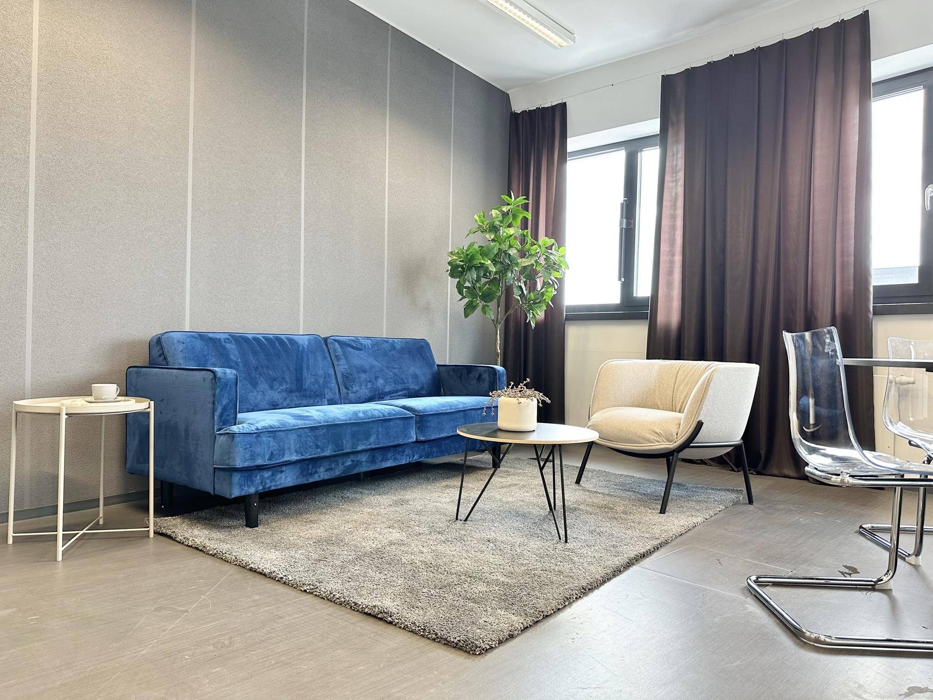 Gemütlicher Loungebereich mit blauem Sofa, Sessel und Beistelltischen in einem modernen Büro.