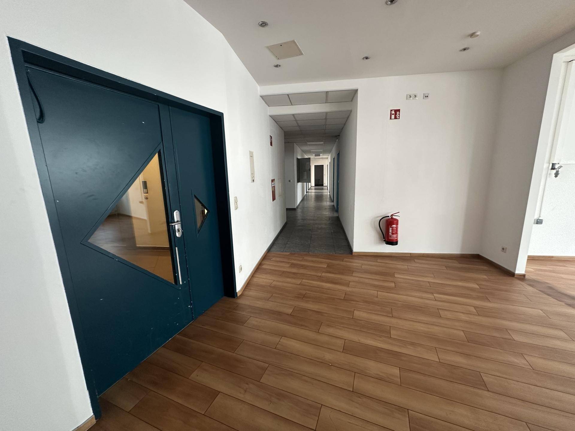 Langer Flur mit Holzboden und Türen zu Büroräumen, ausgestattet mit Feuerlöscher.