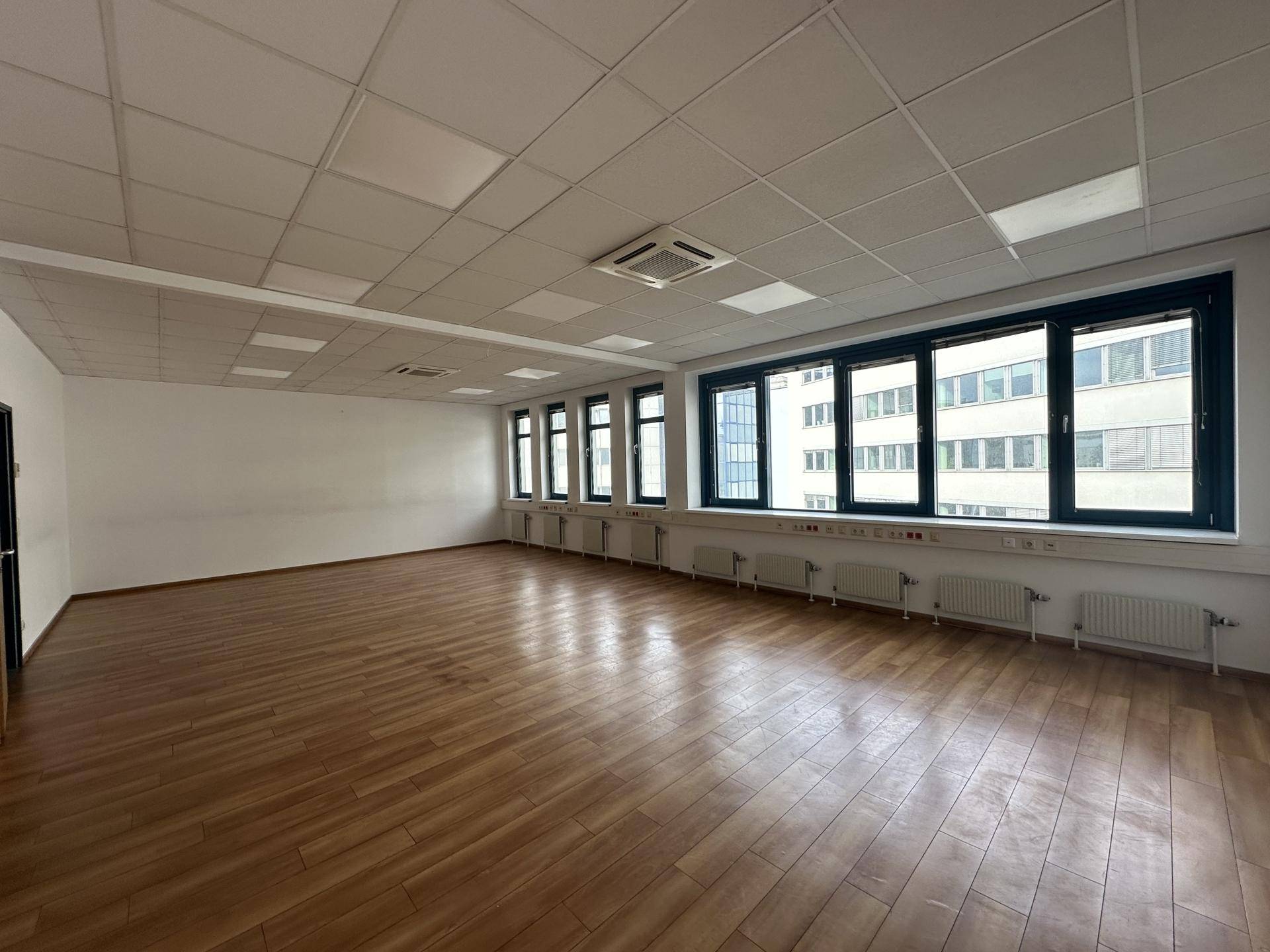 Großzügiger Büroraum mit Holzboden, vielen Fenstern und Deckenbeleuchtung.
