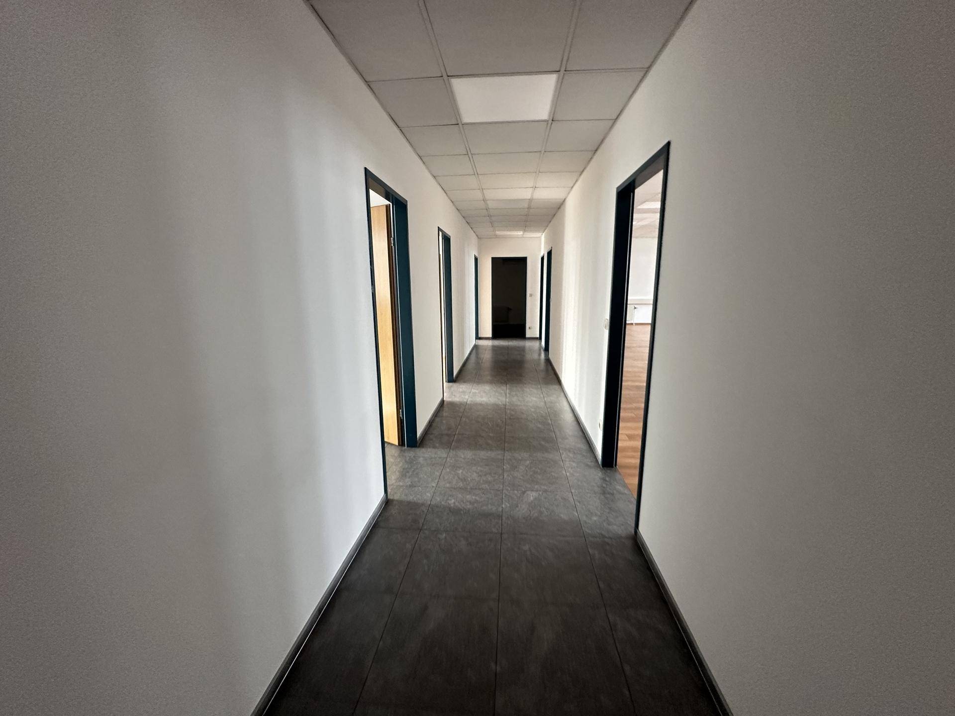 Langer, schmaler Flur mit dunklen Fliesen und mehreren Türen zu Büroeinheiten.