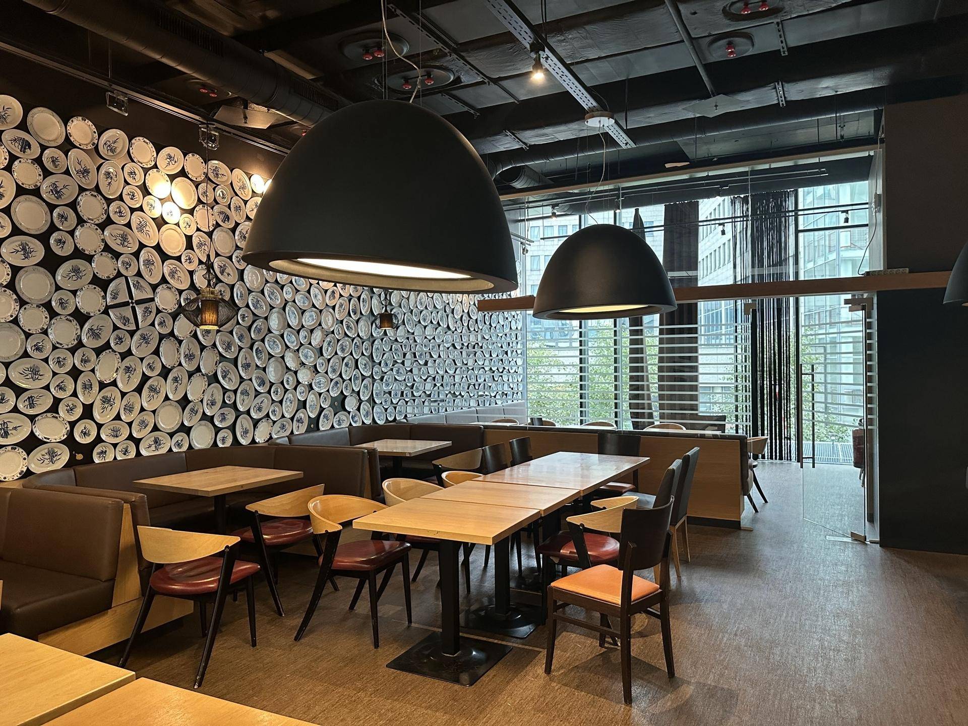 Gemütlicher Restaurant-Essbereich mit verschiedenen Sitzgelegenheiten, dekorativer Tellerwand und großen Pendelleuchten.