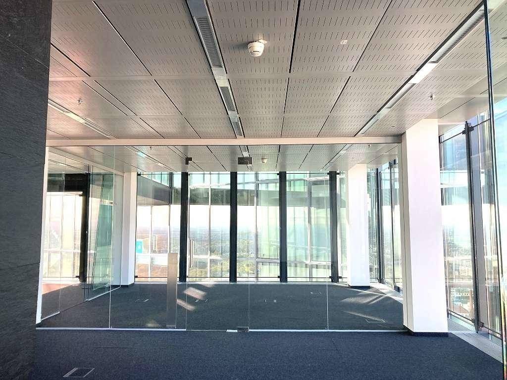Geräumiger, leerer Bürobereich mit raumhohen Glasfenstern und moderner Deckenbeleuchtung.