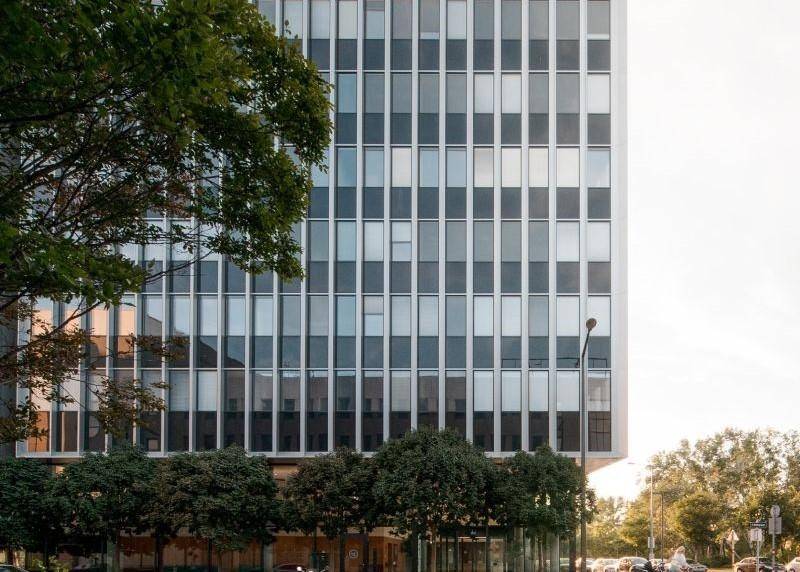 Detailansicht der modernen Fassade eines Bürogebäudes mit vielen Fenstern und Bäumen.