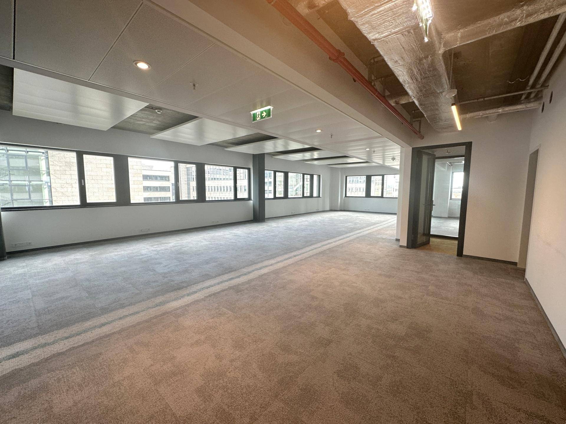 Großes, offenes Büro mit Teppichboden, vielen Fenstern und Blick auf die Stadt.