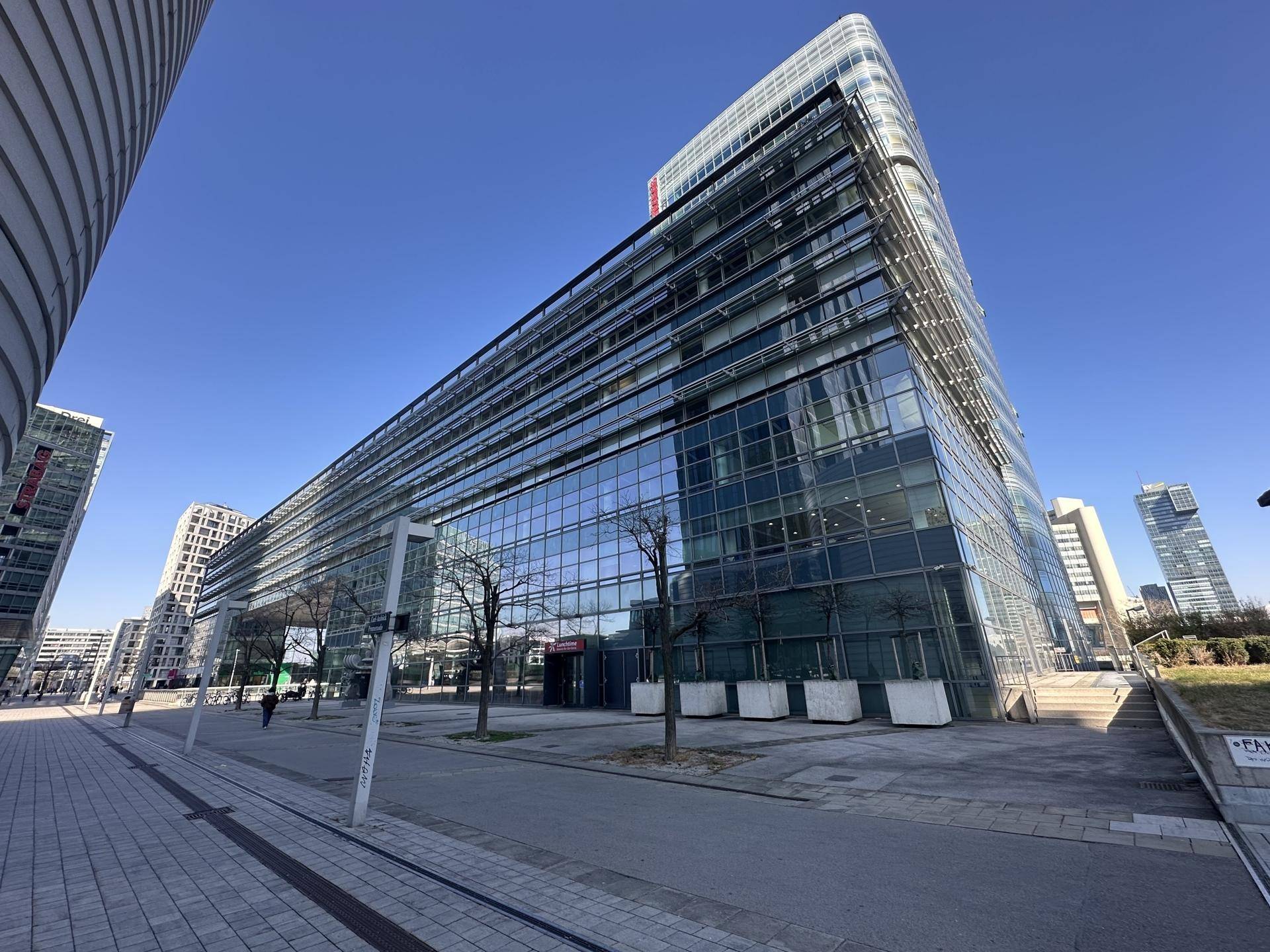 Langes, modernes Bürogebäude mit Glasfassade und klaren Linien unter blauem Himmel.