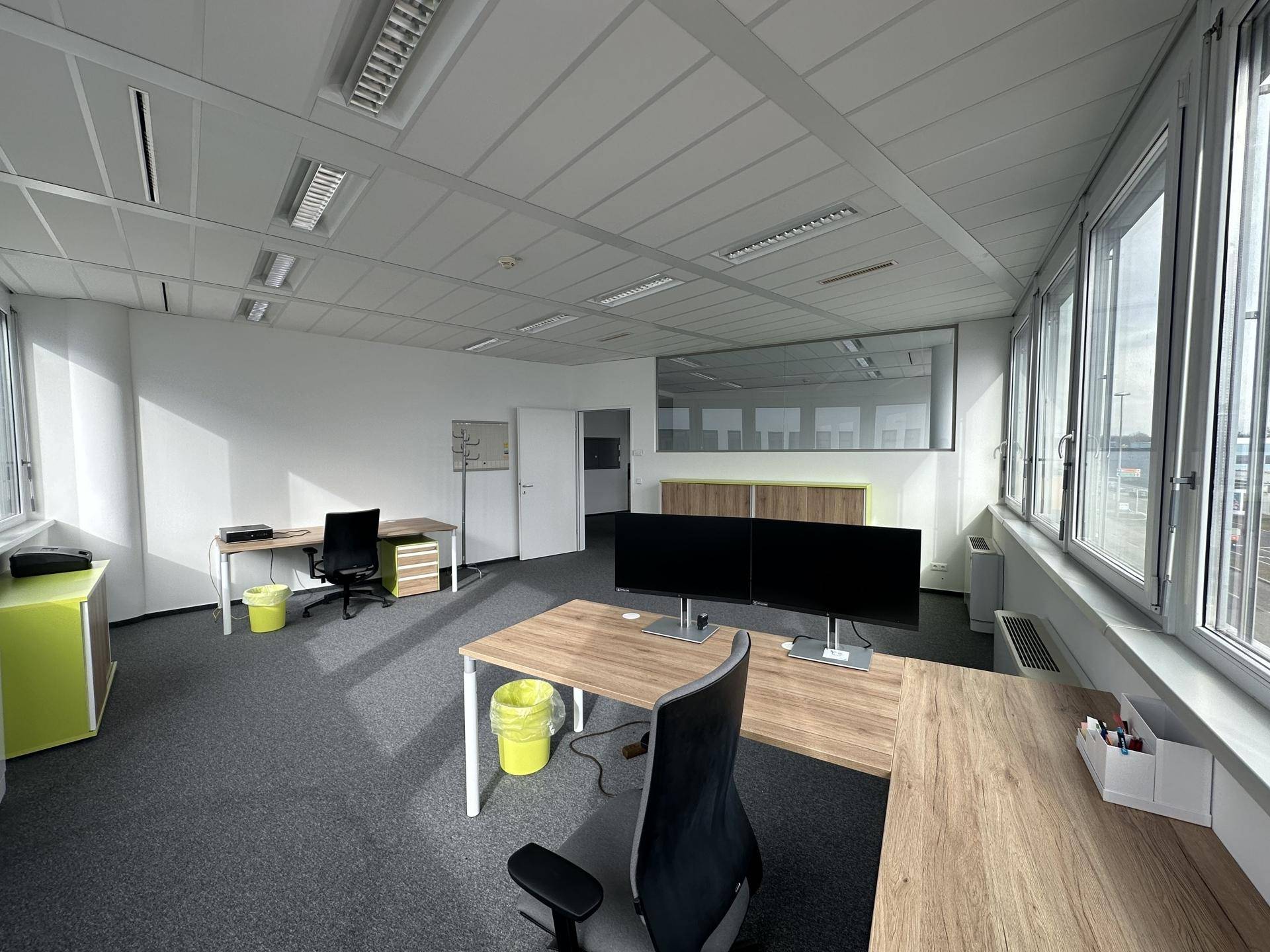 Großes, helles Büro mit mehreren Arbeitsplätzen, Teppichboden und weitem Blick auf die Umgebung durch große Fenster.