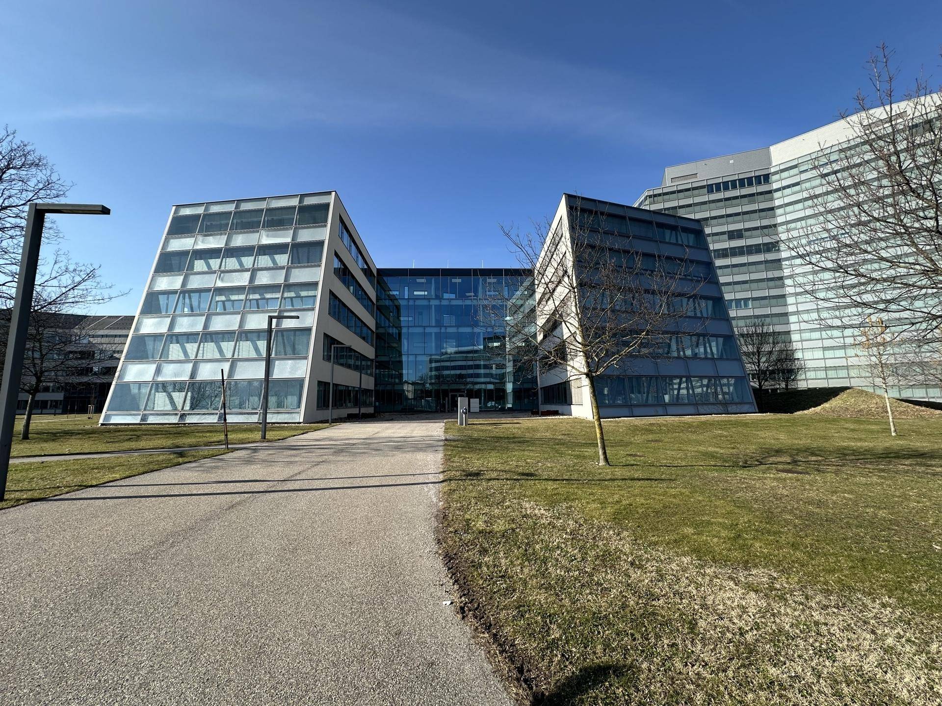 Moderne Bürogebäude mit Glasfassaden und einem gepflegten Weg, umgeben von weitläufigen Grünflächen.