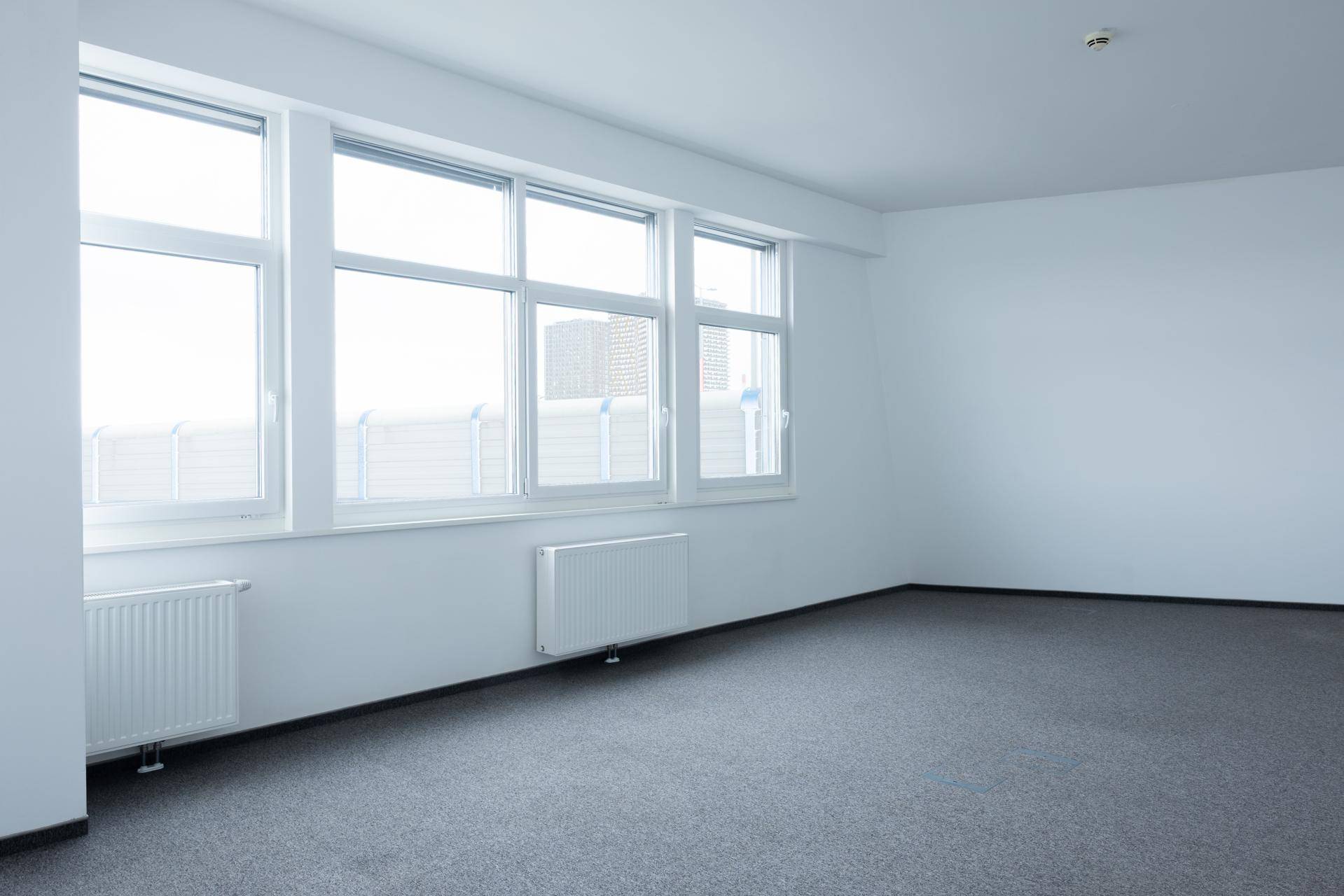Helles Büro mit Teppichboden, großen Fenstern und Heizkörpern unter den Fensterbänken.