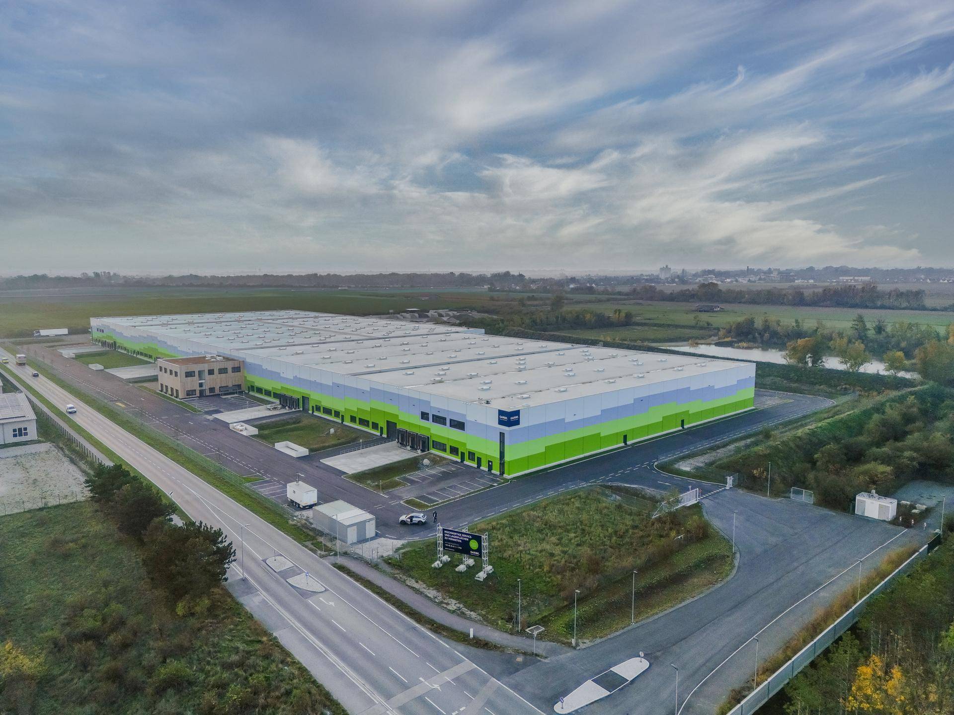 Weitläufiges Logistikzentrum in ländlicher Umgebung mit angrenzenden Feldern und einem kleinen Teich.