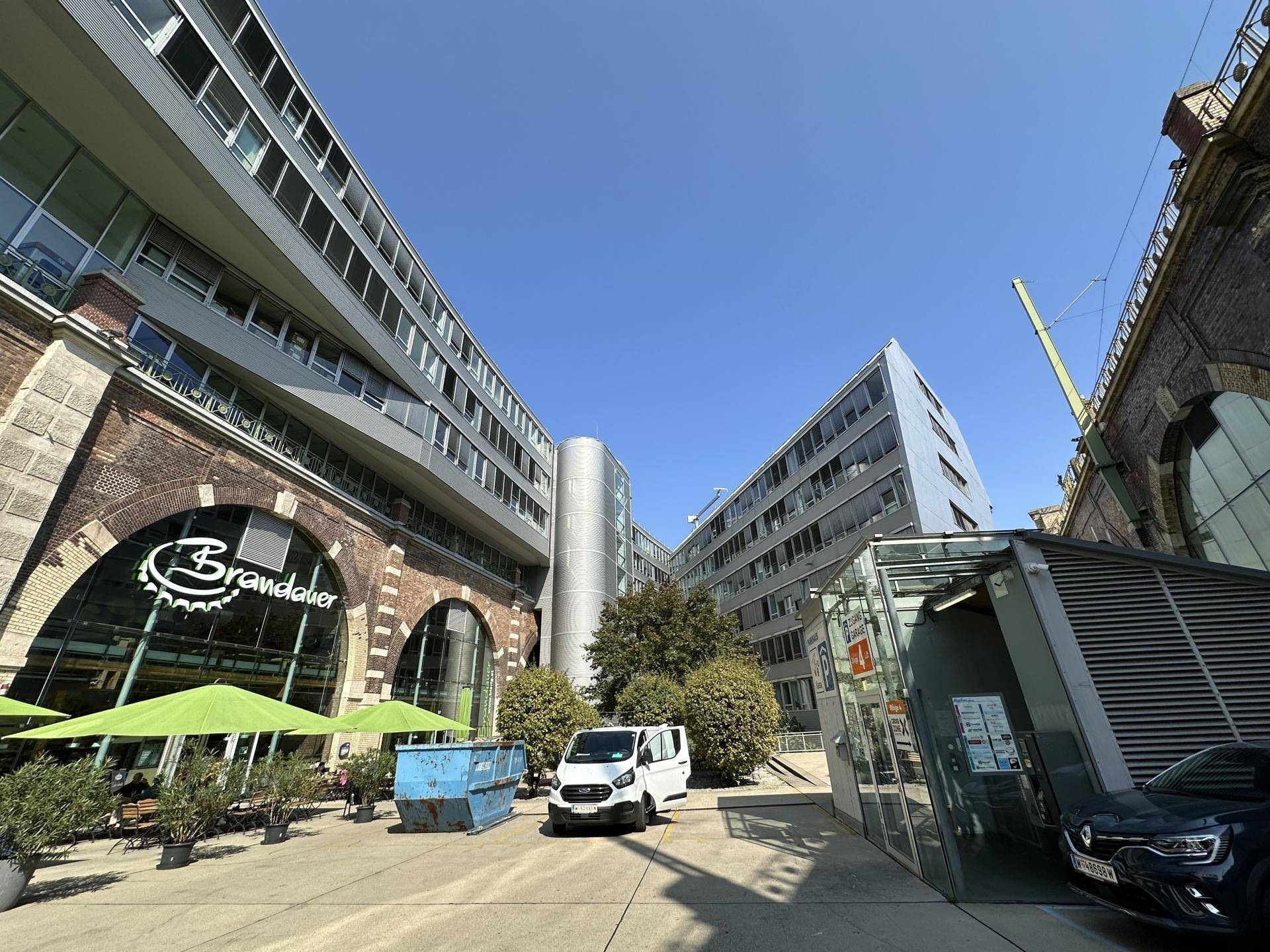 Innenhofbereich mit modernen Bürogebäuden, historischen Backsteinbögen und Grünflächen.