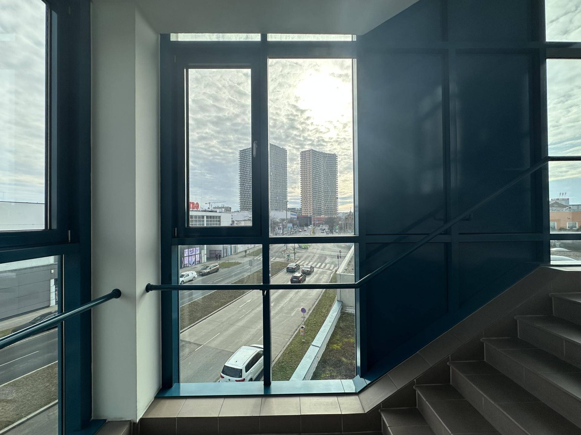 Treppenhaus mit großen Fenstern, die einen Blick auf die Stadt und Hochhäuser bieten.