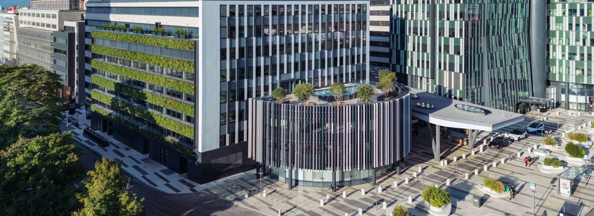 Panoramablick auf einen modernen Gebäudekomplex mit grünen Fassaden und einem runden Gebäude mit Dachbegrünung.