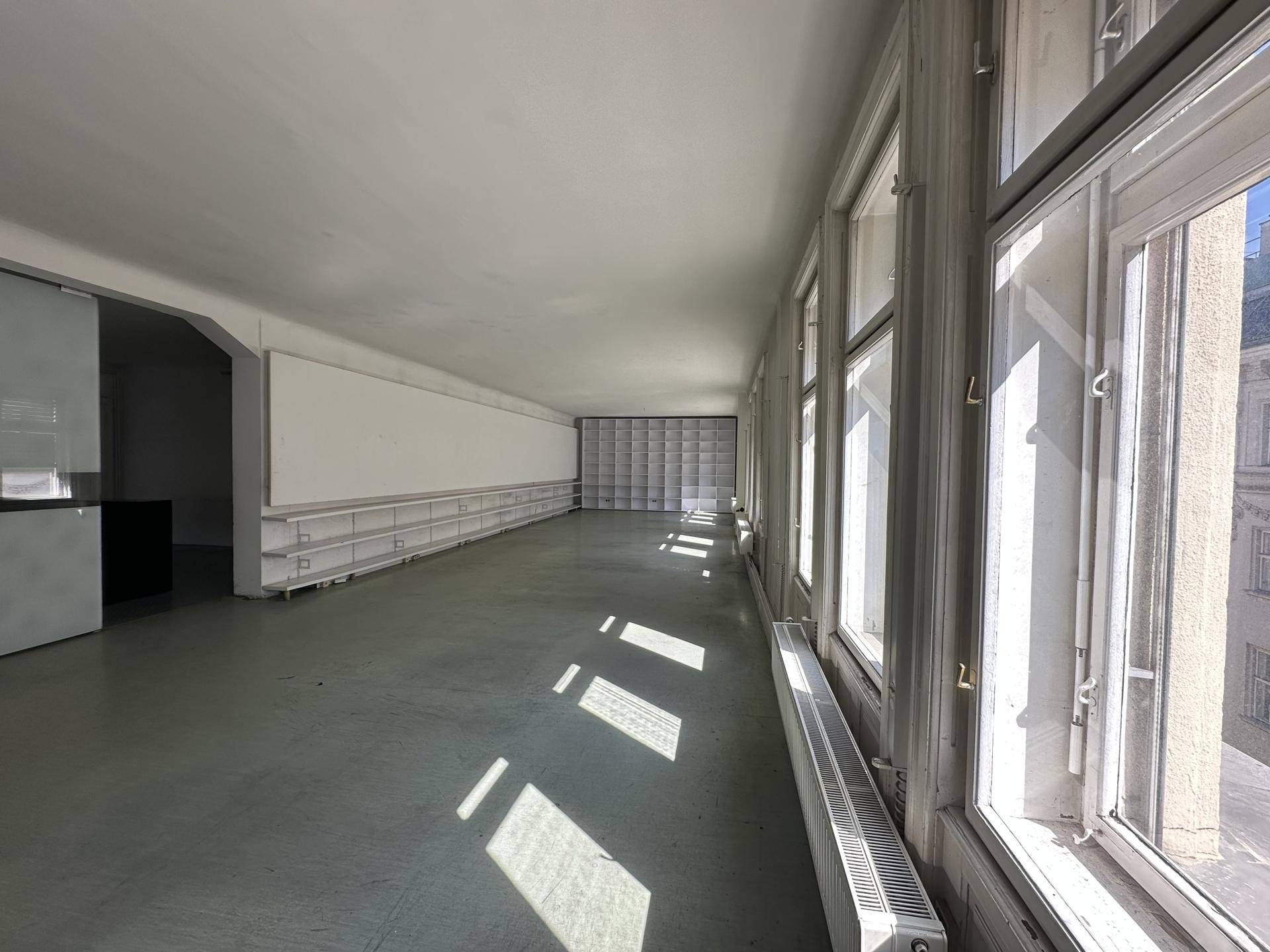 Langer, heller Büroraum mit vielen Fenstern und Regalen entlang der Wand, ideal für Arbeitsplätze.