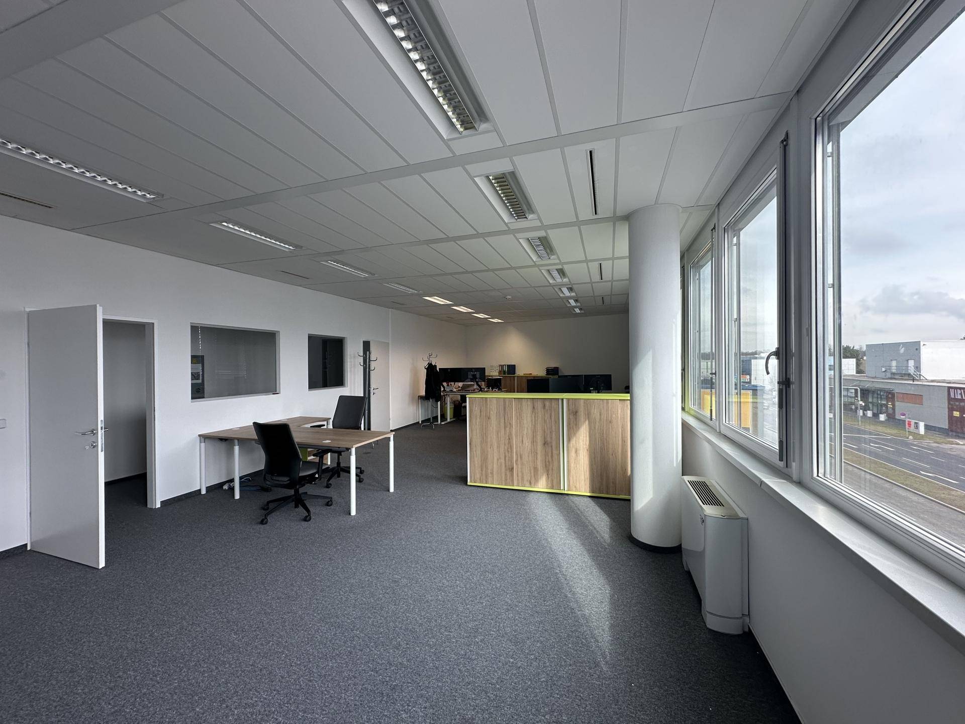 Offener Bürobereich mit Teppichboden, großen Fenstern und Säulen, die den Raum strukturieren und viel Licht hereinlassen.