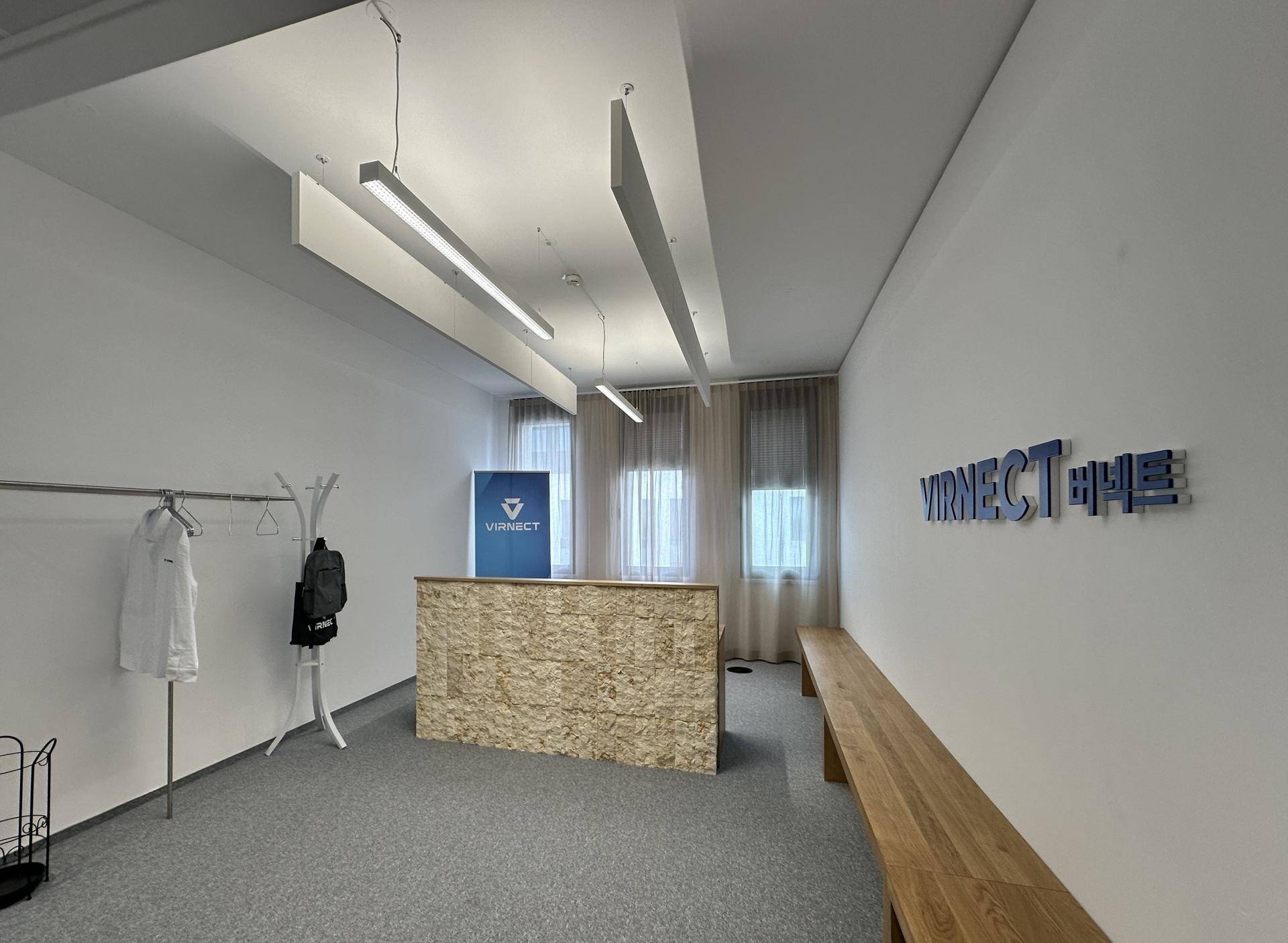 Empfangsbereich mit Holztresen, grauen Teppichböden und einer langen Holzbank, ideal für Besucher.