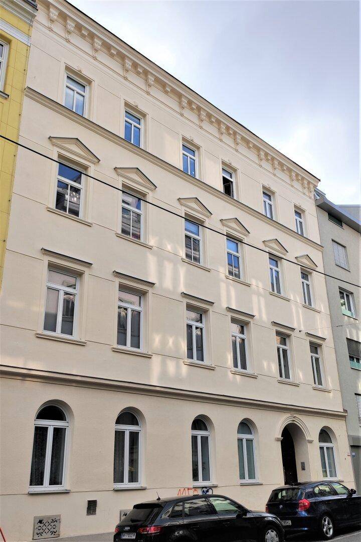 Historisches Gebäude mit klassischer Fassade, vielen Fenstern und geparkten Autos davor.