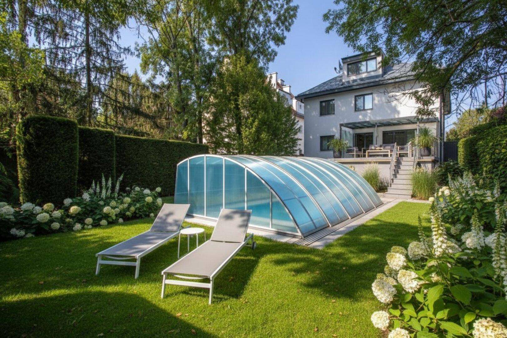 Großer Garten mit Rasenfläche, überdachtem Pool und Liegestühlen, umgeben von Bäumen und Hecken.