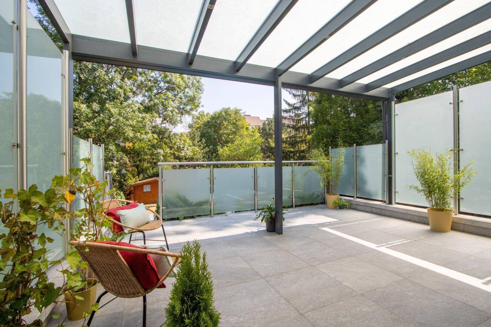Geräumige Terrasse mit Überdachung und Glasabtrennungen, bietet einen weiten Blick ins Grüne.