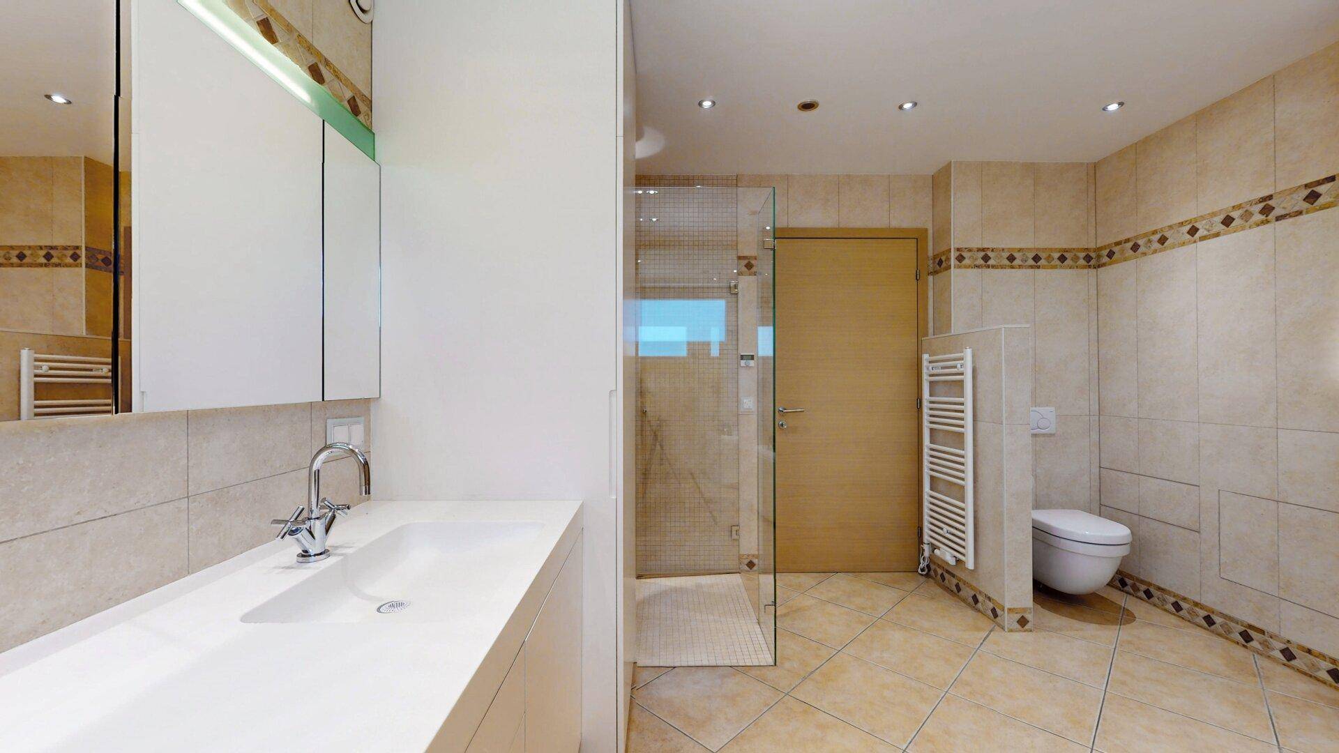 Geräumiges Badezimmer mit Dusche, Einzelwaschbecken und beheiztem Handtuchhalter, in beigen Fliesen.