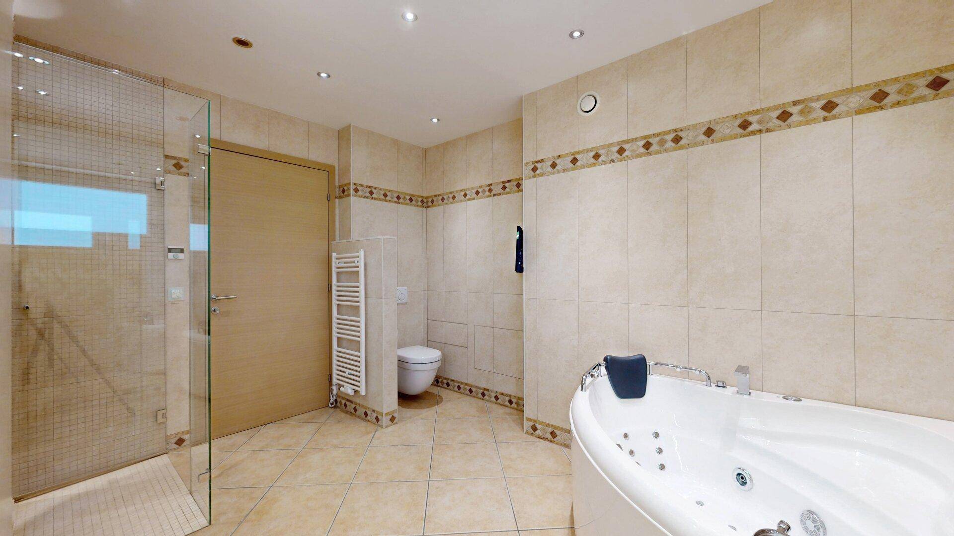 Großes Badezimmer mit Whirlpool-Badewanne, Dusche und beheiztem Handtuchhalter, in beigen Fliesen.