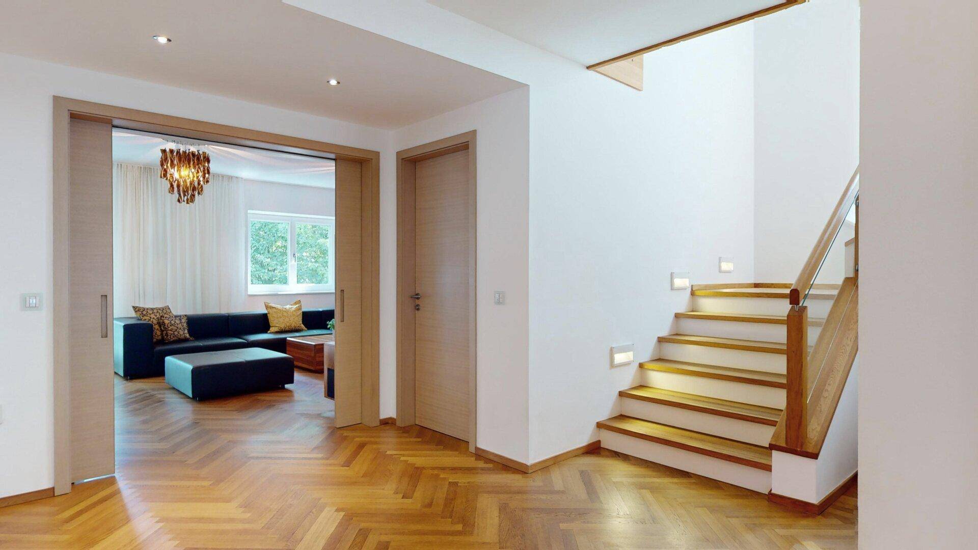 Eingangsbereich mit Fischgrätparkett und einer Holztreppe, die in die oberen Etagen führt.