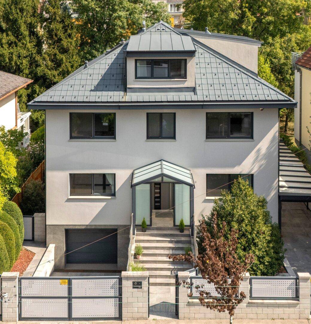 Ansicht der modernen Stadtvilla mit Mansarddach, Garage und gepflegtem Vorgarten.