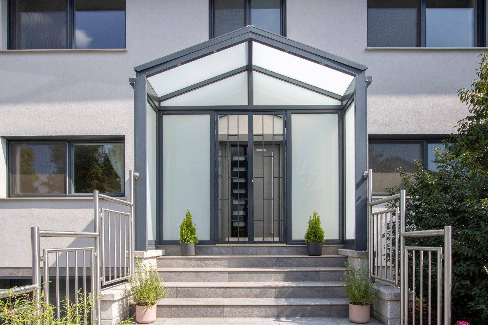 Eingangsbereich der Villa mit überdachtem Portal, Treppe und modernem Geländer.