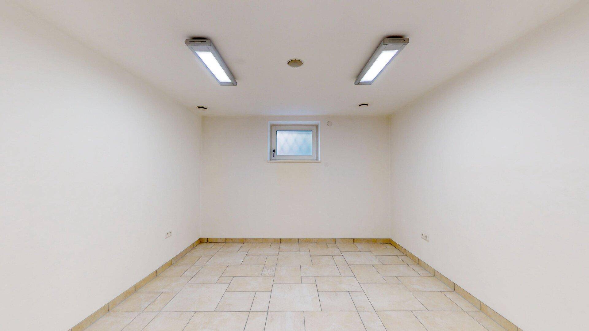 Kleiner Kellerraum mit Fliesenboden und Fenster, ideal als Abstellraum oder Hobbyraum.