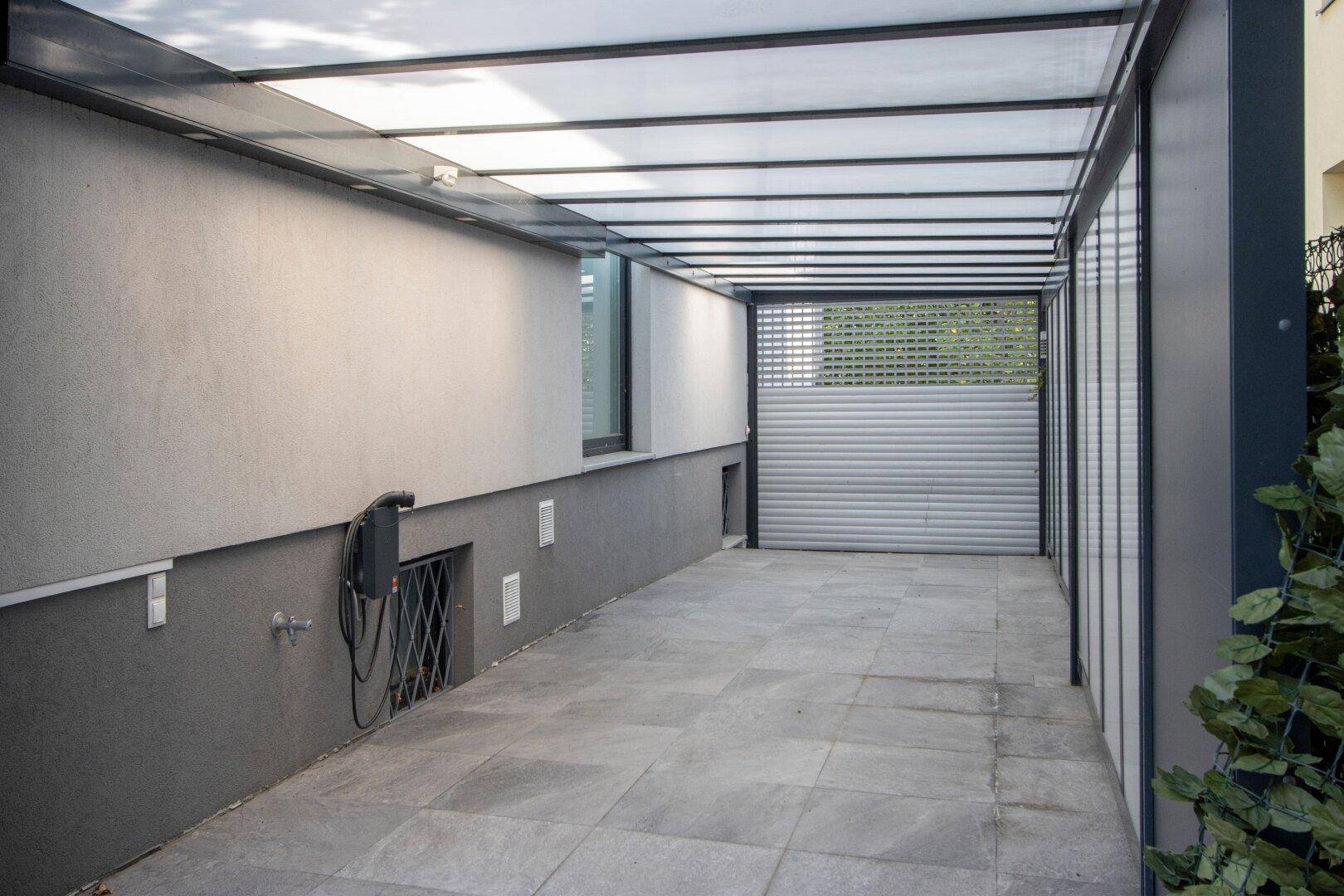 Überdachter Carport mit Fliesenboden und EV-Ladestation, bietet geschützten Stellplatz.