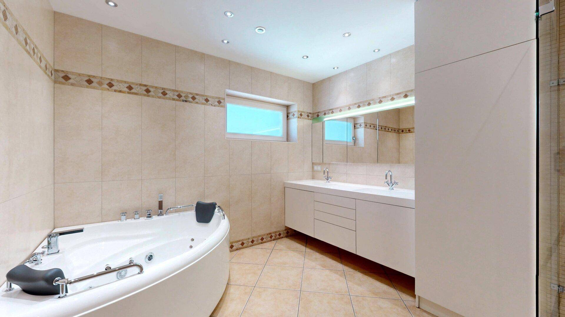 Geräumiges Badezimmer mit Whirlpool-Badewanne, Doppelwaschbecken und Einbauschrank, in beigen Fliesen.