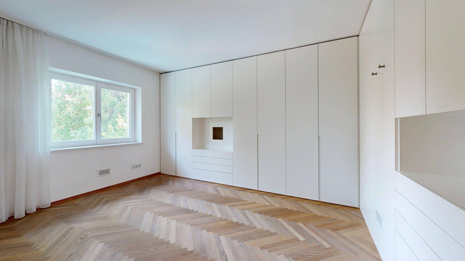 Unmöbliertes Schlafzimmer mit Fischgrätparkett und großen Einbauschränken, bietet viel Stauraum.