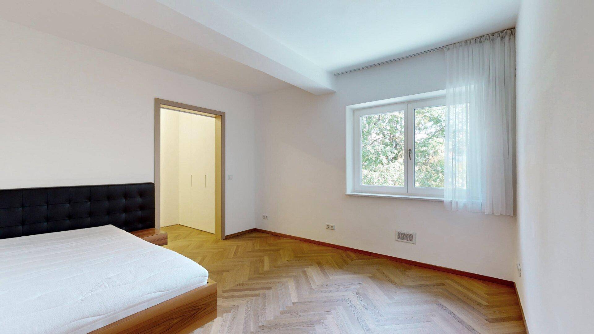 Helles Schlafzimmer mit Fischgrätparkett und Fenster mit Blick ins Grüne.