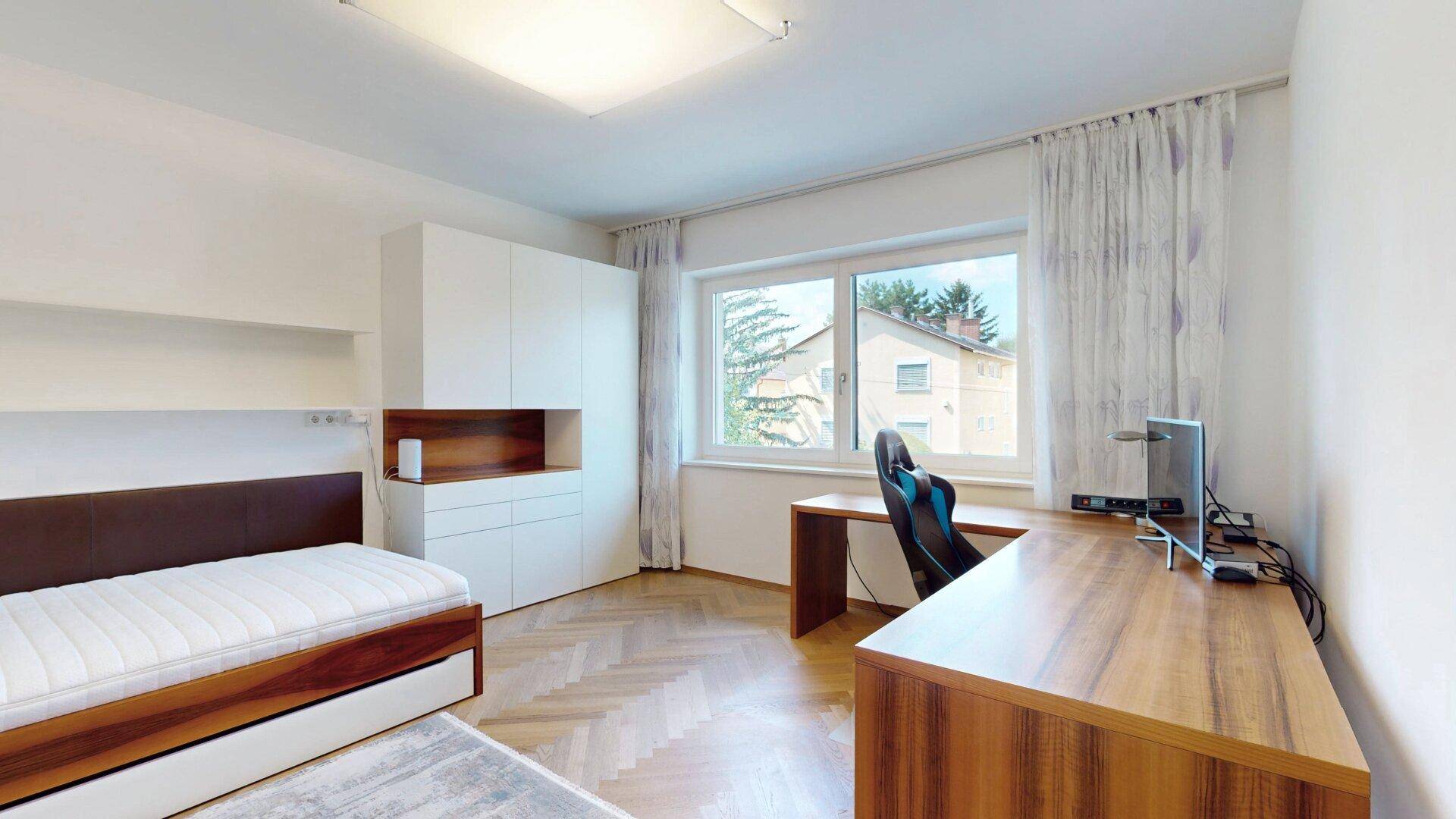 Geräumiges Schlafzimmer mit Fischgrätparkett, Schreibtisch und Blick ins Grüne.