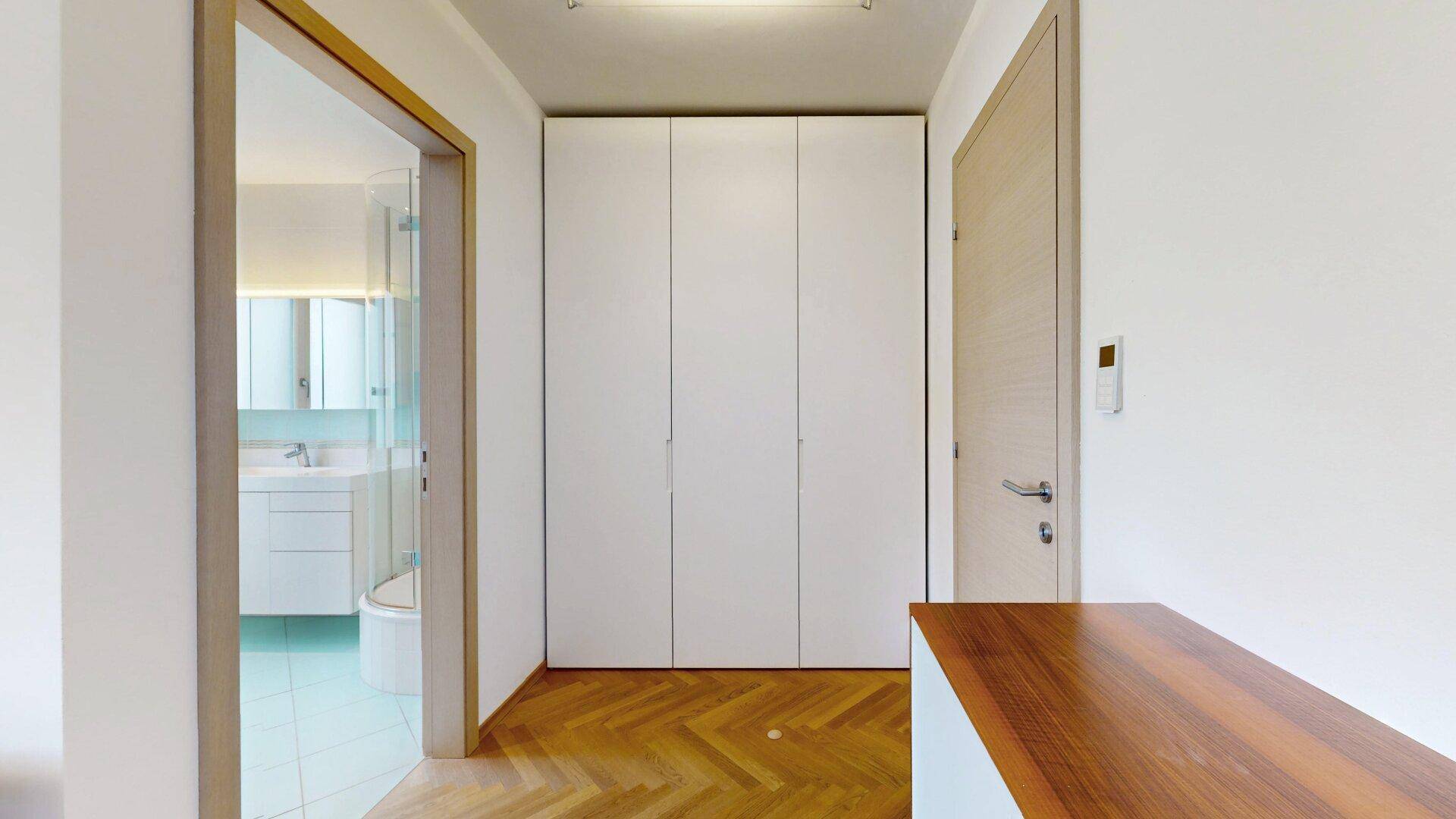 Flur mit Fischgrätparkett und Einbauschränken, führt zu einem modernen Badezimmer.