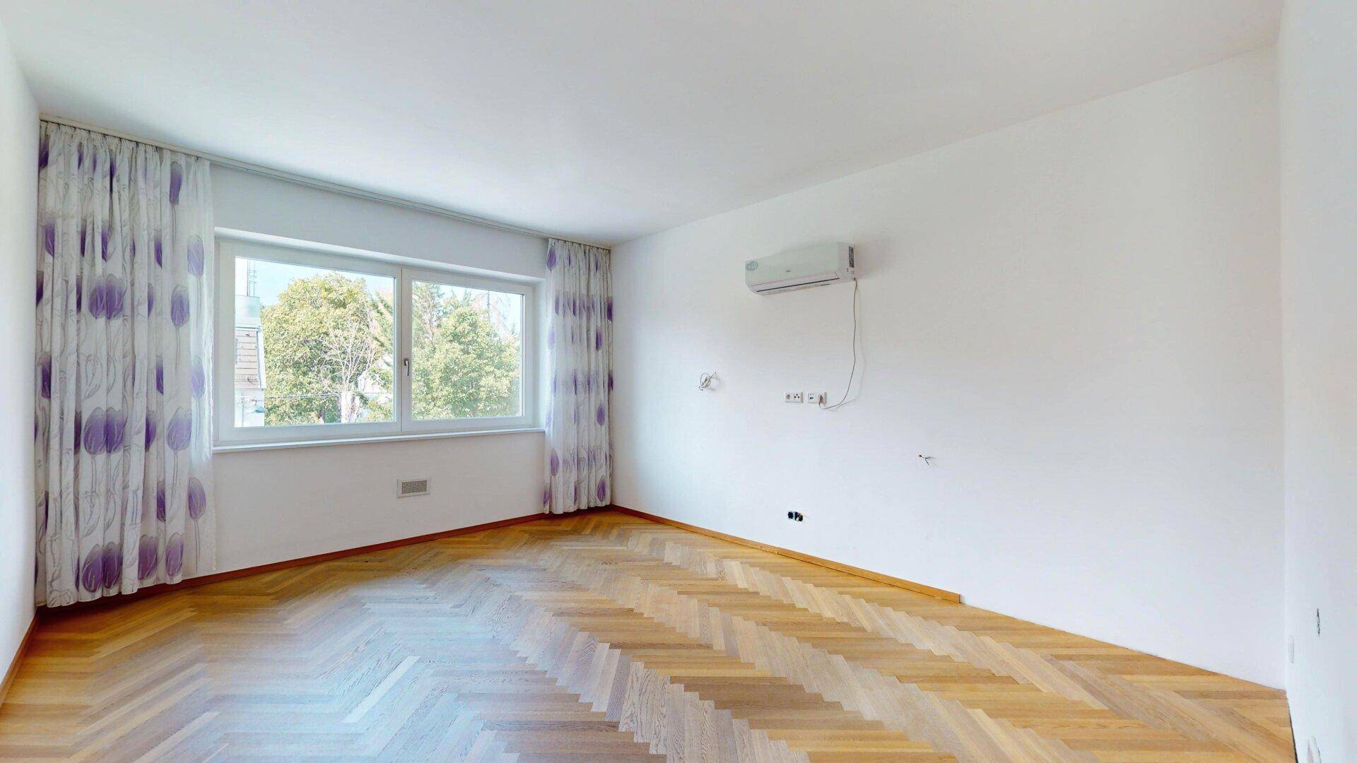 Unmöbliertes Schlafzimmer mit Fischgrätparkett, großem Fenster und Klimaanlage.