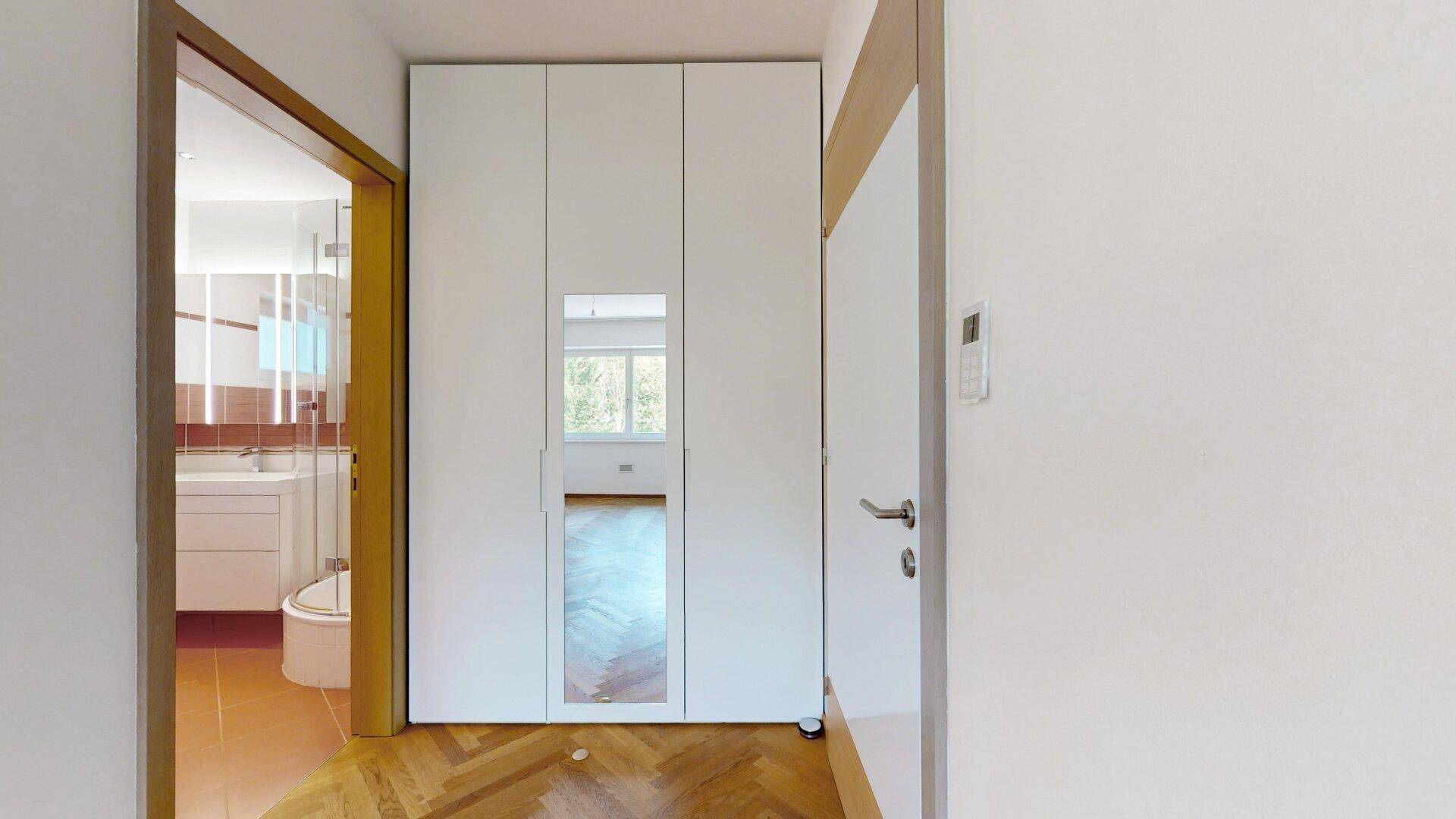 Flur mit Fischgrätparkett und Einbauschrank, führt zu einem Badezimmer mit roten Akzenten.